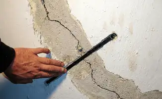 A wall with a large crack is being inspected by a professional in Pasadena, CA